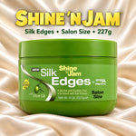 A green jar of Shine 'N Jam Silk Edges salon size hair product, displayed on a draped champagne satin background with the brand name and product details printed above.