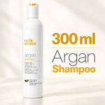 A white bottle of Milk Shake Argan Shampoo stands on a light beige surface with soft shadows. Large text on the right reads '300 ml Argan Shampoo' in yellow and gray.