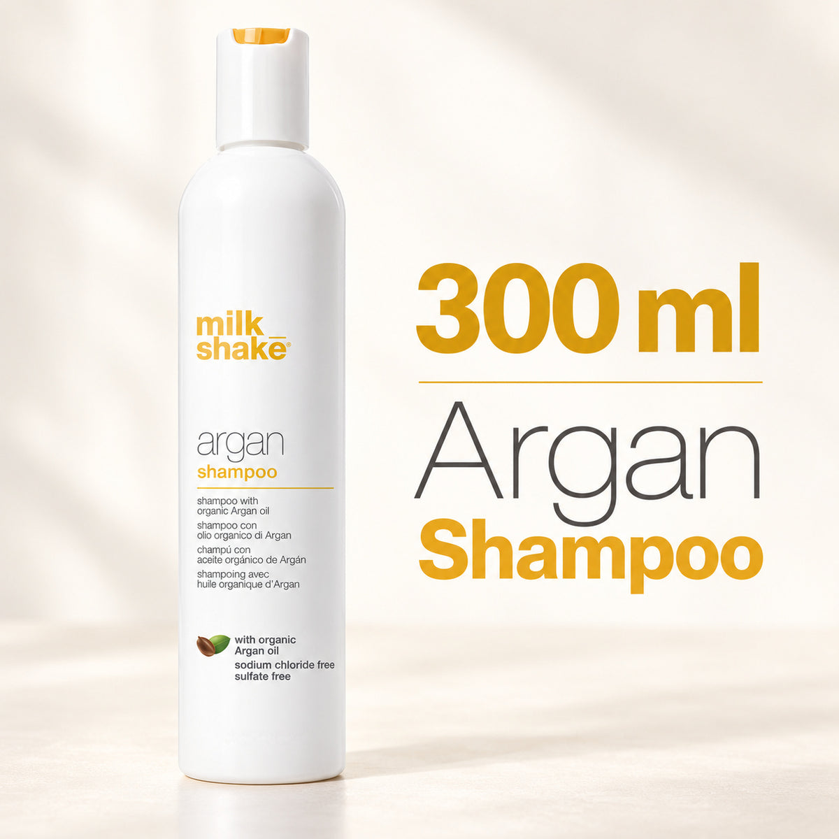 A white bottle of Milk Shake Argan Shampoo stands on a light beige surface with soft shadows. Large text on the right reads '300 ml Argan Shampoo' in yellow and gray.